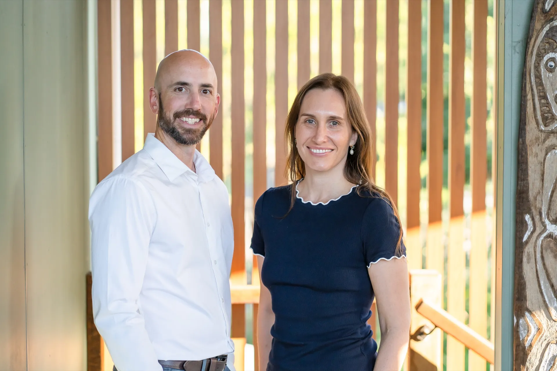 Two clinicians standing together by a sunlit timber screen