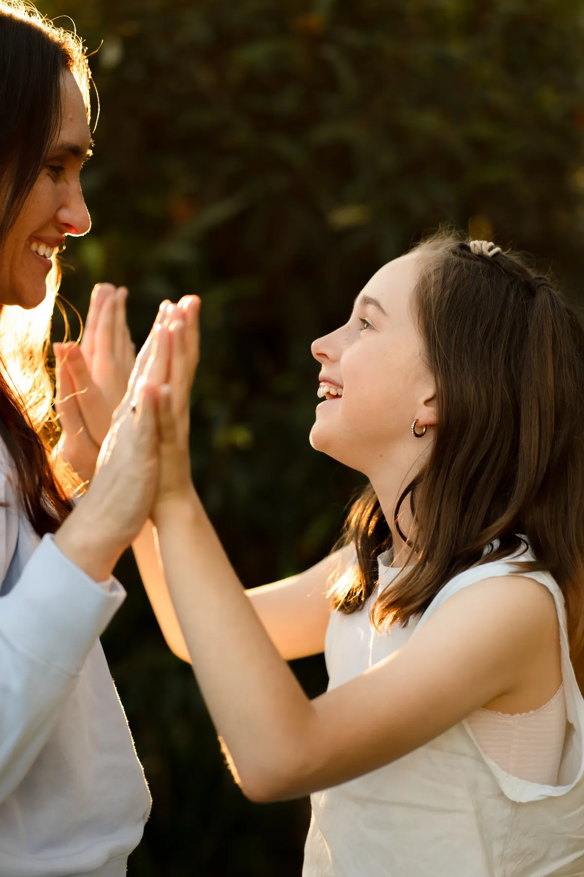 An adult and a child playing a hand-clapping game together at golden hour