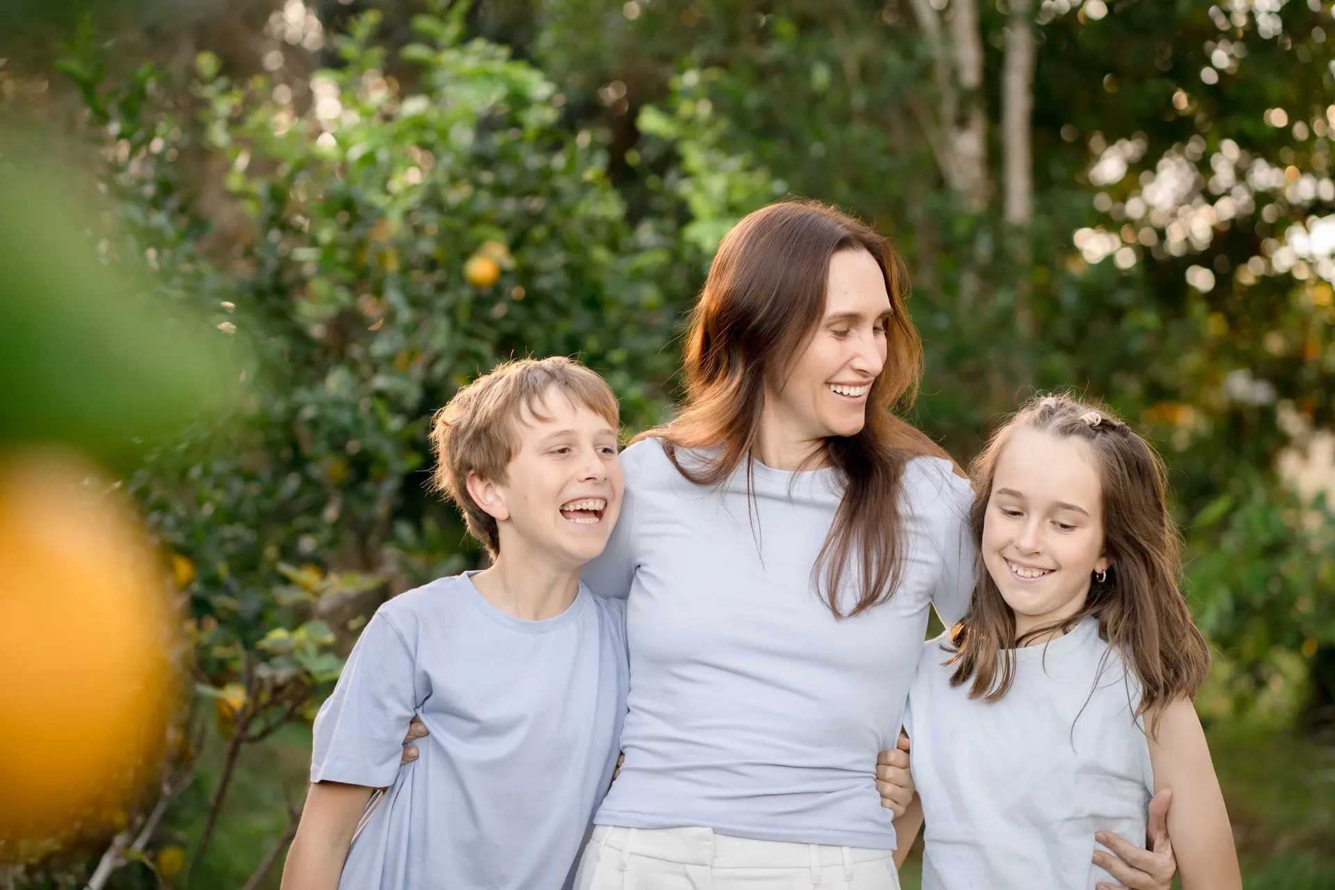 A parent and two children smiling together outdoors among orange trees